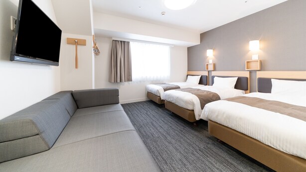 Habitación de hotel con televisor de pantalla plana grande, sofá, dos camas individuales y un escritorio pequeño.