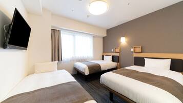 Une chambre d’hôtel avec trois lits, un téléviseur à écran plat, une fenêtre avec des rideaux et un luminaire fixé au mur.