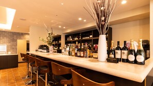 Una zona de bar con una barra larga, varios taburetes y una amplia selección de botellas.
