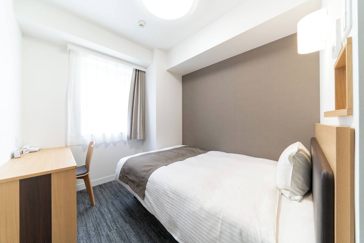 A hotel room with a bed, a desk, a chair, and a window with curtains.