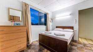 A bedroom with a wooden bed, a dresser, a window with curtains, and a mirror on the wall.