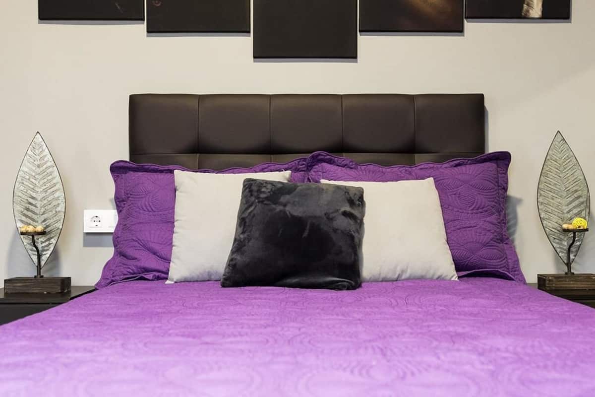 A bed with a purple bedspread and a black pillow, flanked by two nightstands with decorative items.