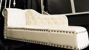 Un canapé blanc recouvert de tissu, doté d’un dossier capitonné et de boutons décoratifs, placé contre un mur sombre près d’une grande fenêtre.