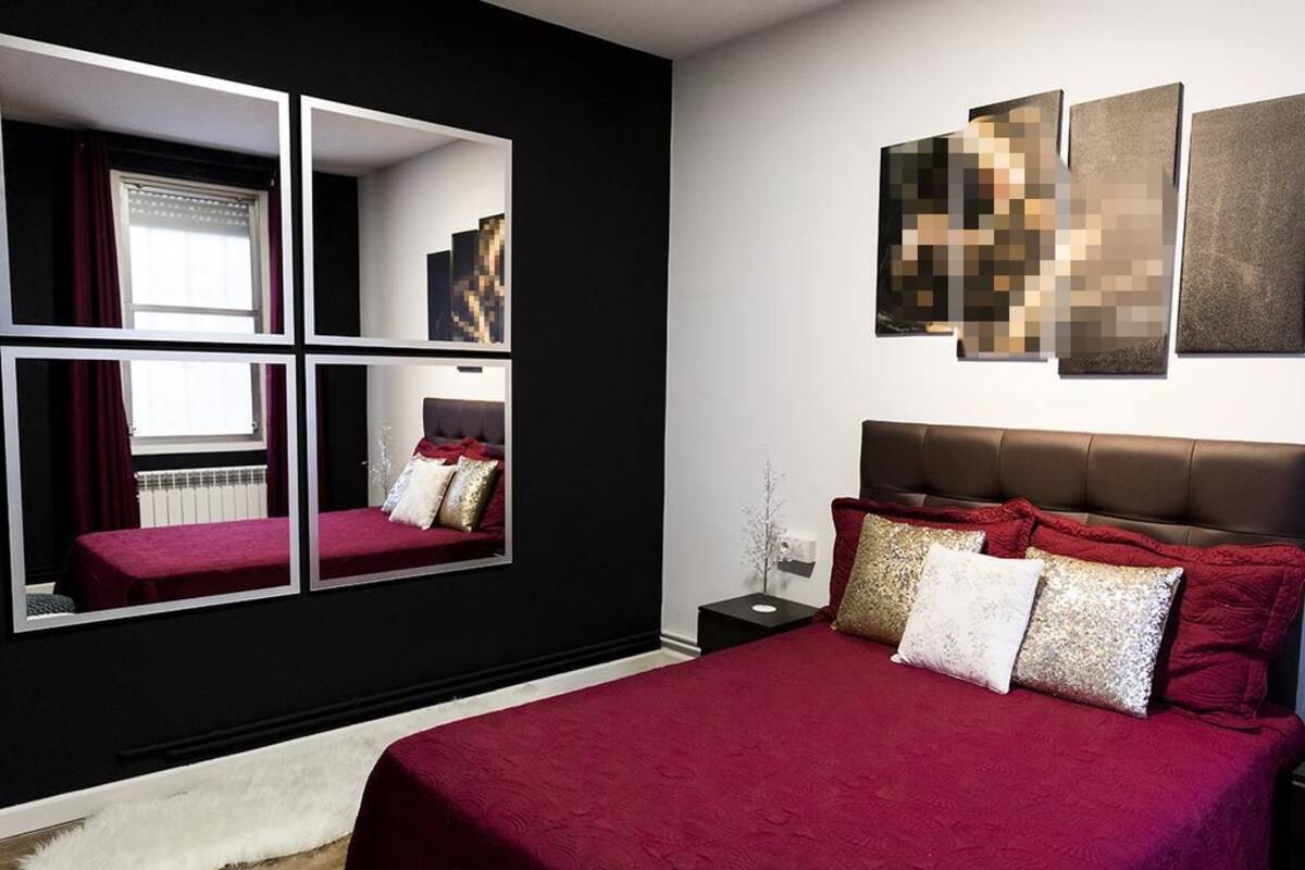 A modern bedroom with a large bed, a nightstand, and a mirror.