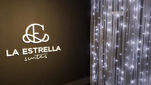 Un mur sur lequel est apposée une enseigne indiquant « LA ESTRELLA suites », et un rideau orné de guirlandes lumineuses verticales.