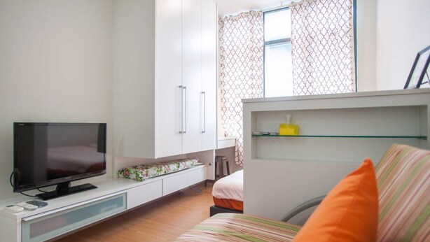 A modern, well-lit room with a flat-screen TV, a bed with striped bedding, a white wardrobe, and a small desk area. - Centrestage - Heart of Petaling Jaya 1 (Petaling Jaya)