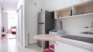 A modern kitchen with white cabinets, a stainless steel refrigerator, a microwave, and a sink. There is a small dining area with a wooden table and red stools. - Centrestage - Heart of Petaling Jaya 1 (Petaling Jaya)