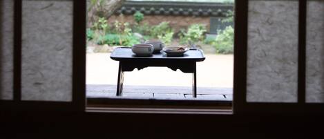 A traditional Japanese room with tatami flooring, a low table with a tea set, and a view of a large tree through a shoji screen.