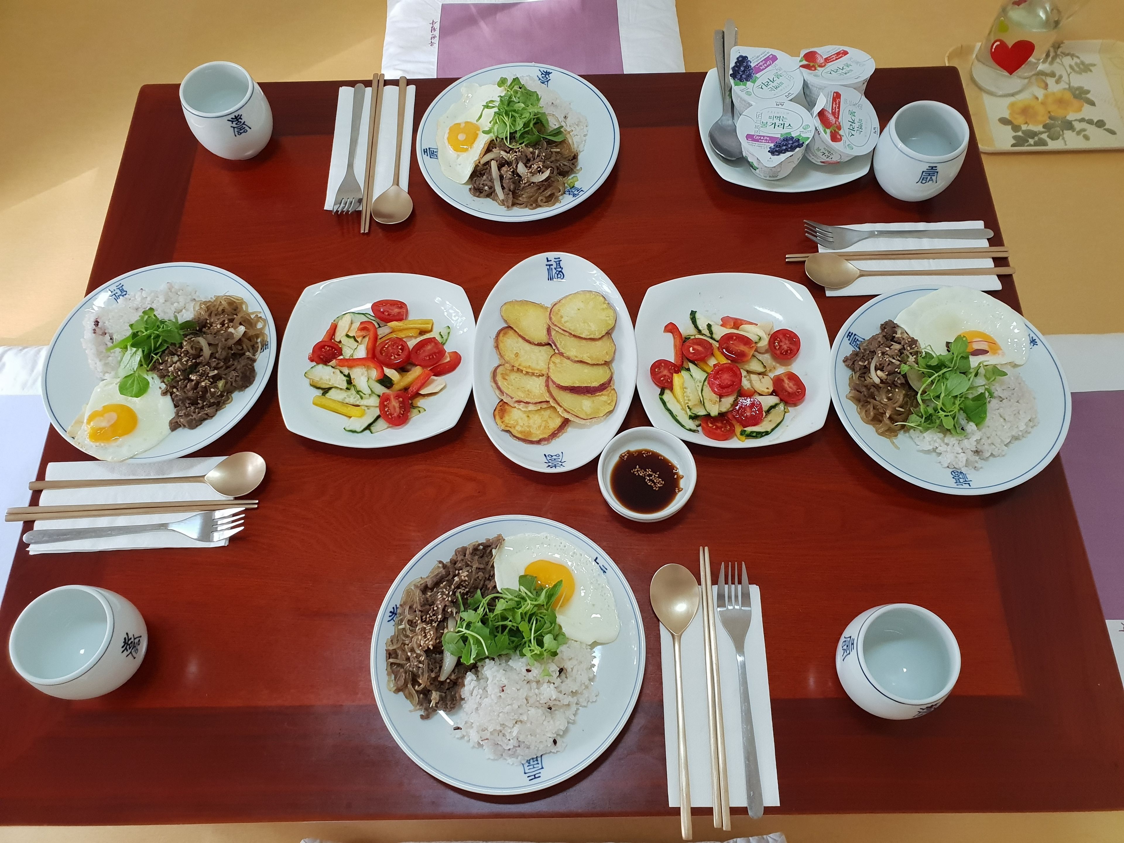 A dining table with multiple plates of food, chopsticks, spoons, and cups.