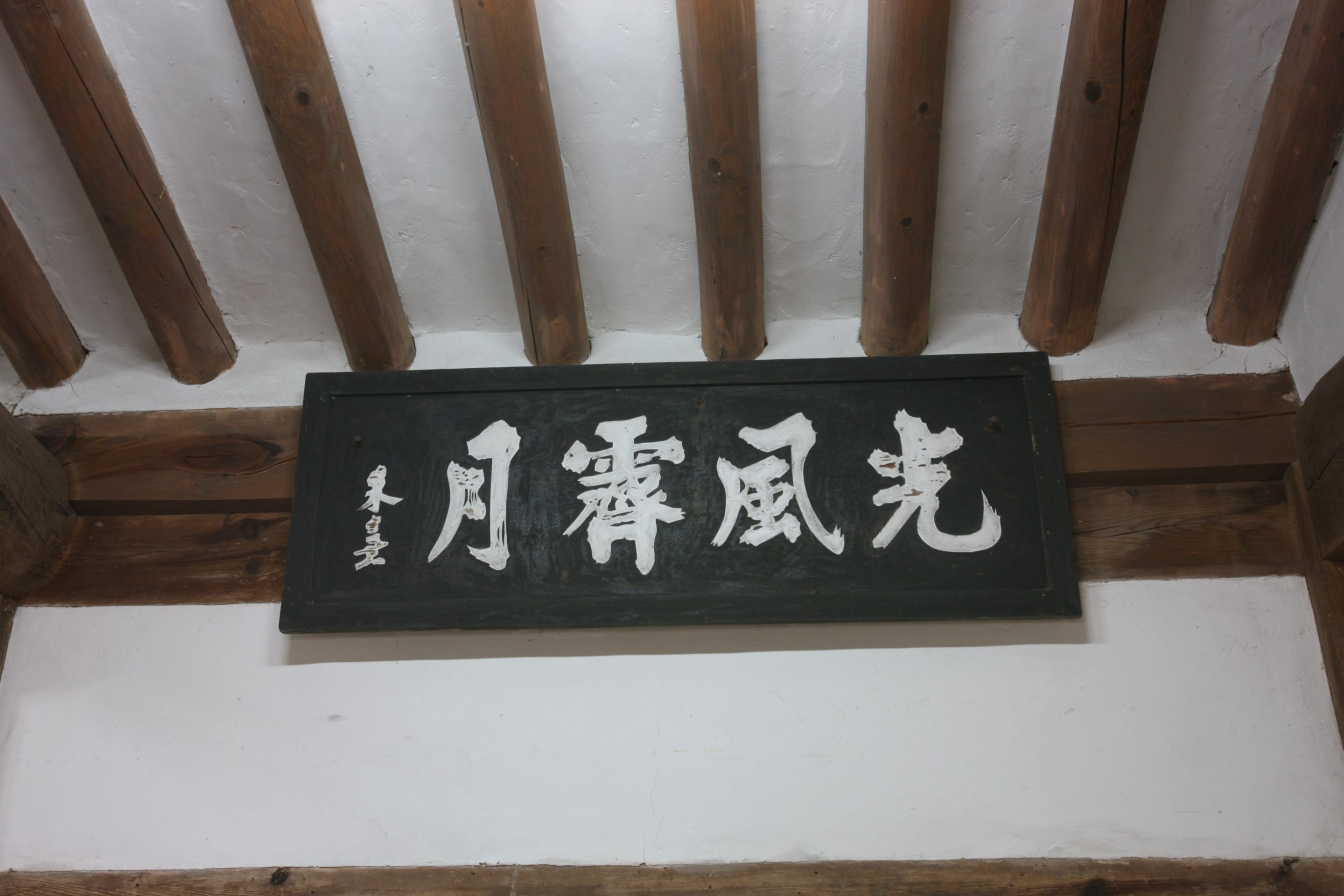 Un letrero negro con caracteres chinos blancos sobre una pared blanca.