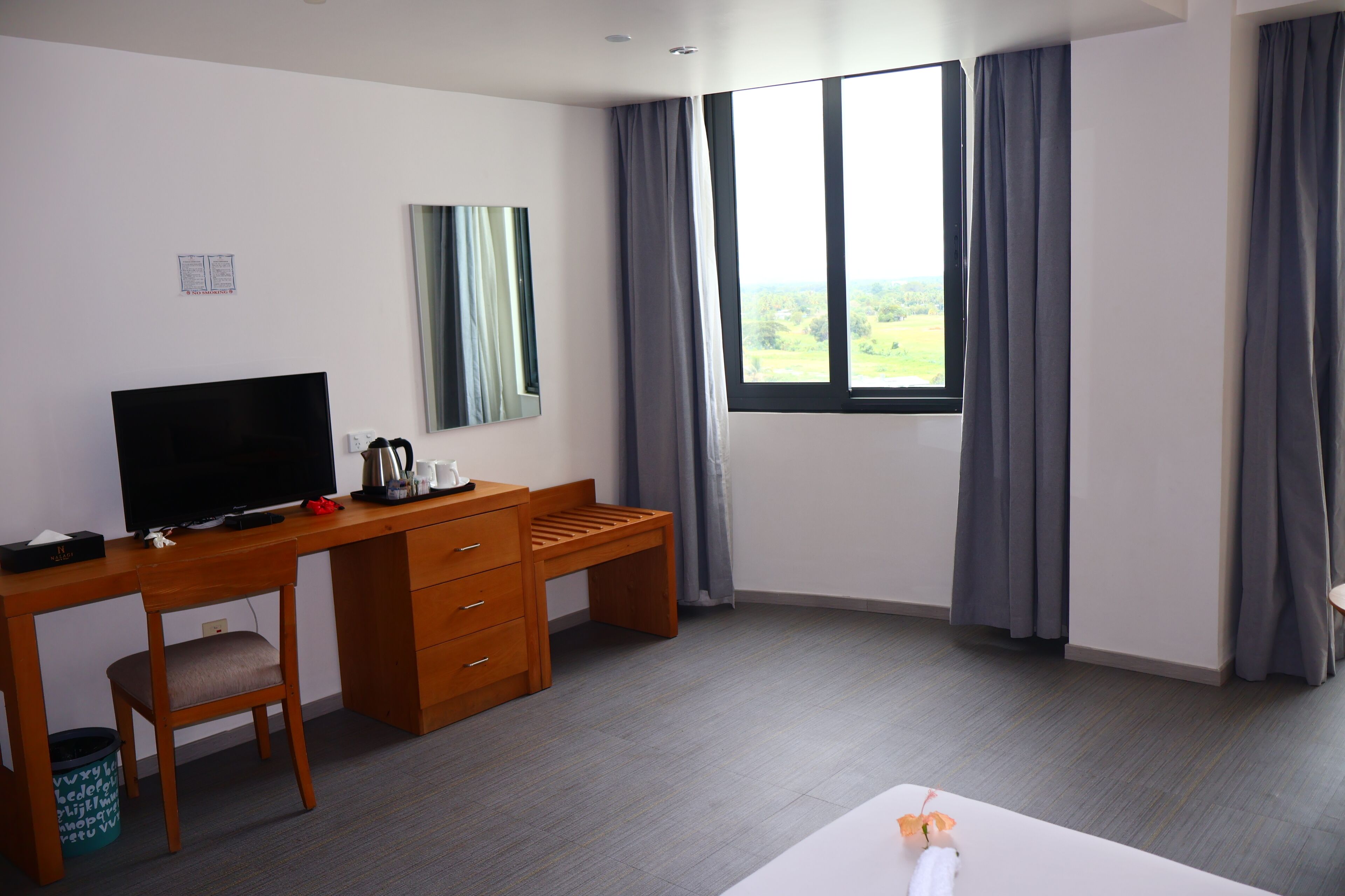A hotel room with a desk, a television, a chair, a bed, and a window with curtains.