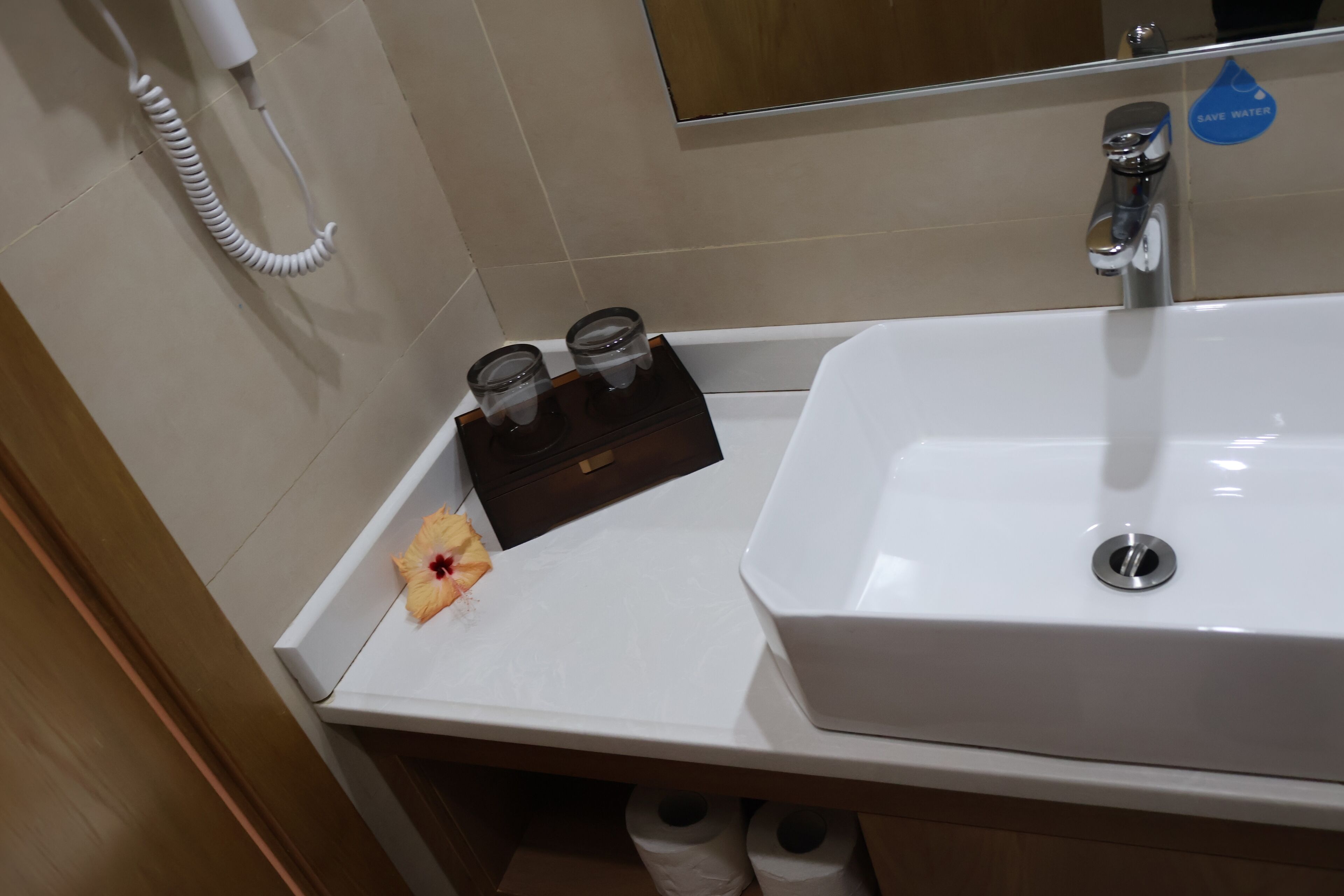 A bathroom with a white sink, a mirror, a towel rack, and a "Save Water" sticker.