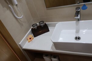 Un baño con lavamanos blanco, espejo, toallero y un adhesivo que dice "Ahorra Agua".
