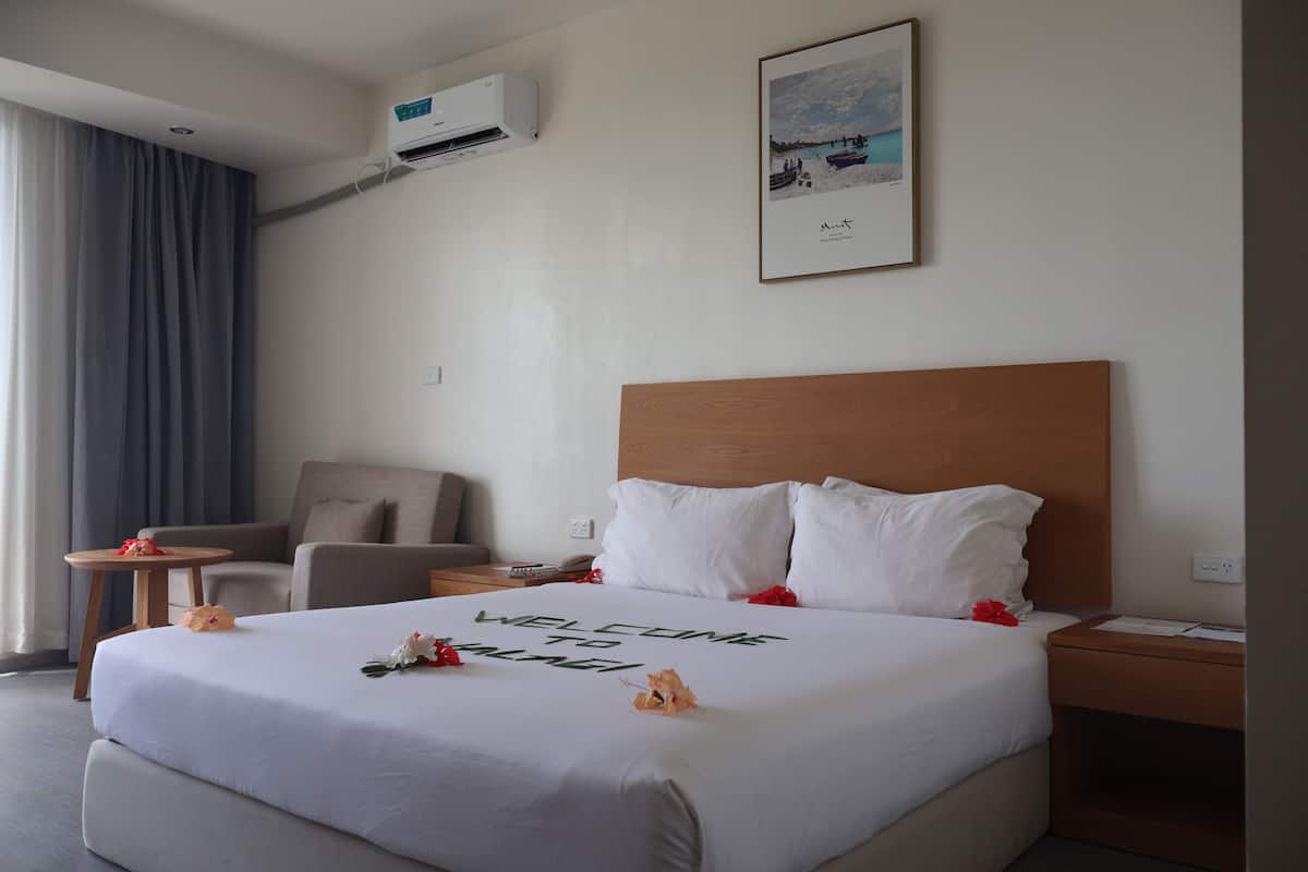 Une chambre d’hôtel avec un grand lit, une tête de lit en bois, une table de chevet, une chaise et un tableau encadré au mur.