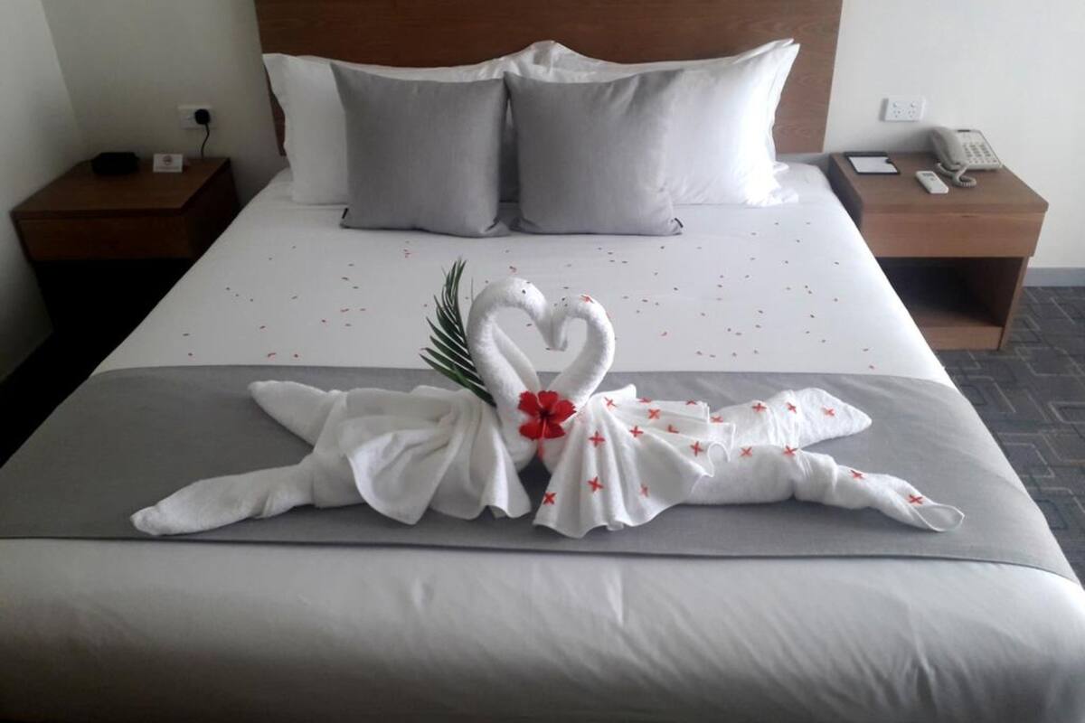 Une chambre d’hôtel avec un lit bien fait, deux tables de chevet, une tête de lit en bois et un téléphone sur la table de chevet à droite.