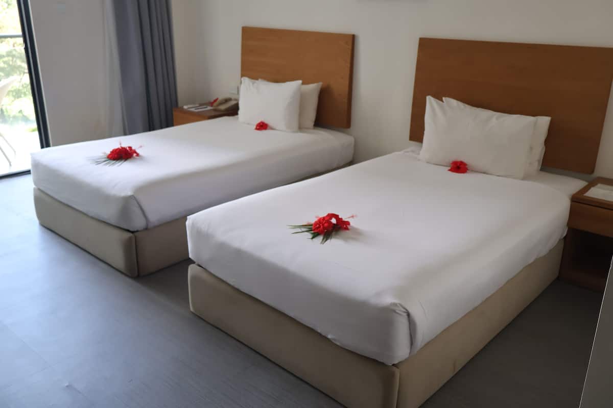 Deux lits bien faits, avec du linge de lit blanc et des fleurs rouges, des têtes de lit en bois et un plancher en bois.