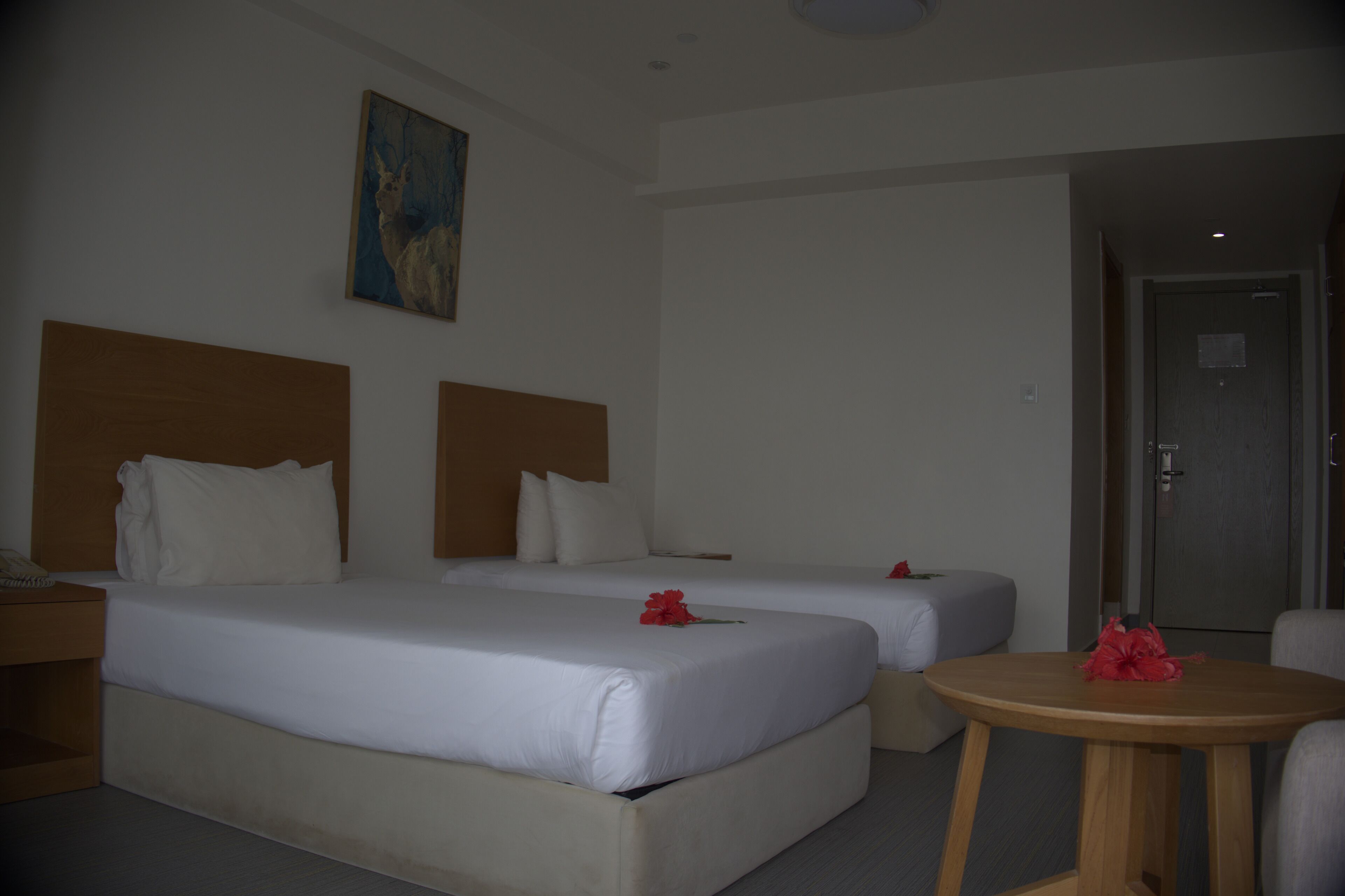 A hotel room with two beds, a wooden headboard, a small round table, and a painting on the wall.