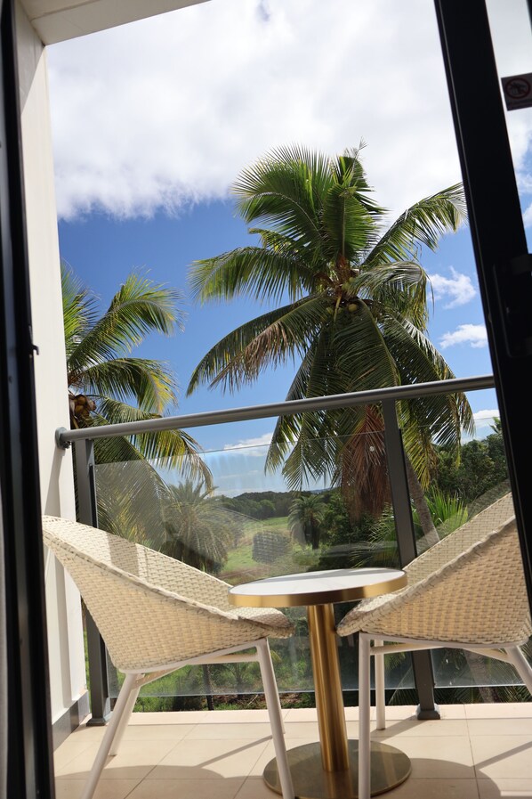 A balcony with two wicker chairs and a round table, overlooking palm trees and a clear blue sky. - Nalagi Hotel (Nadi)