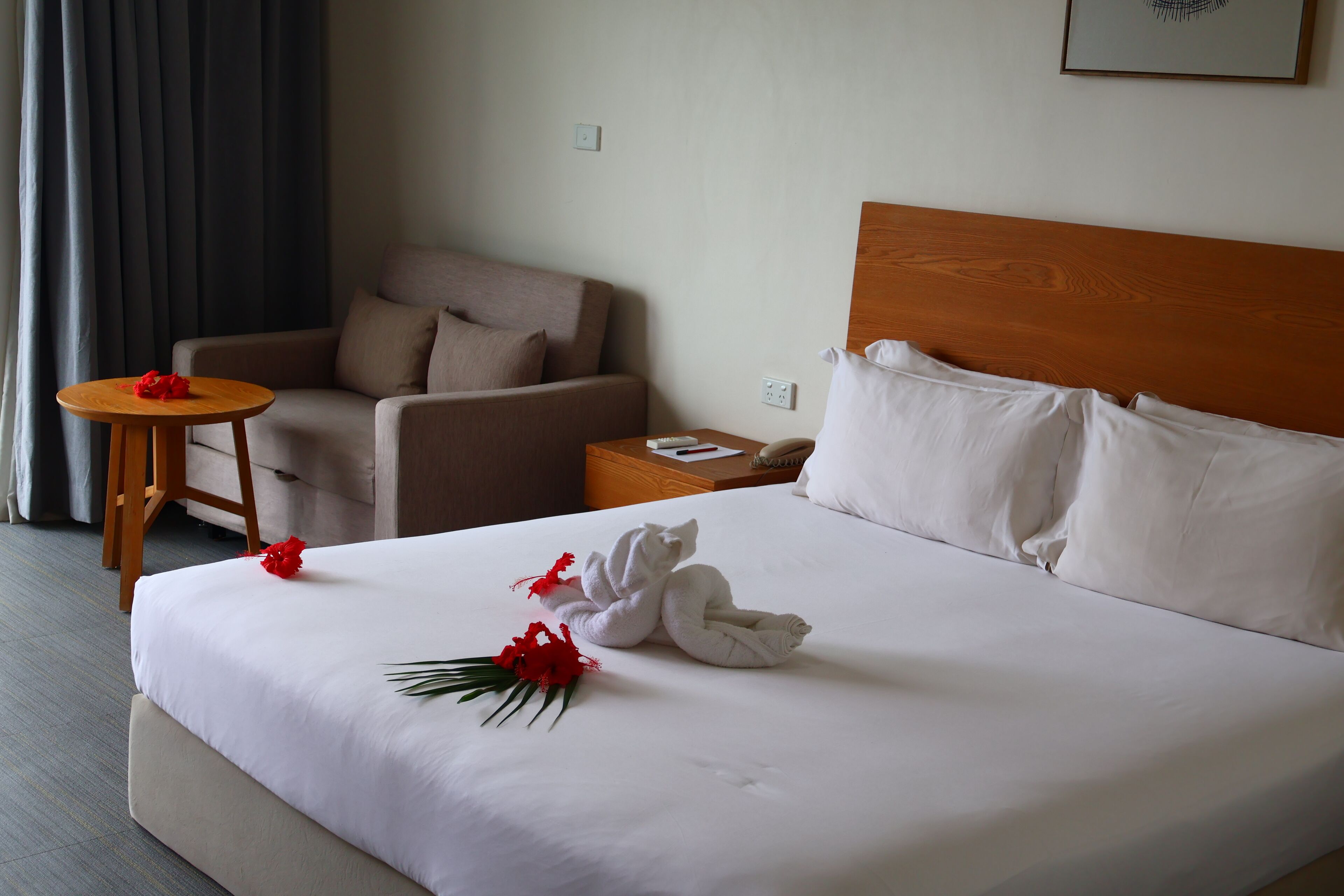 Habitación de hotel con una cama bien hecha, un cabecero de madera, una mesita de noche con lámpara y una silla.