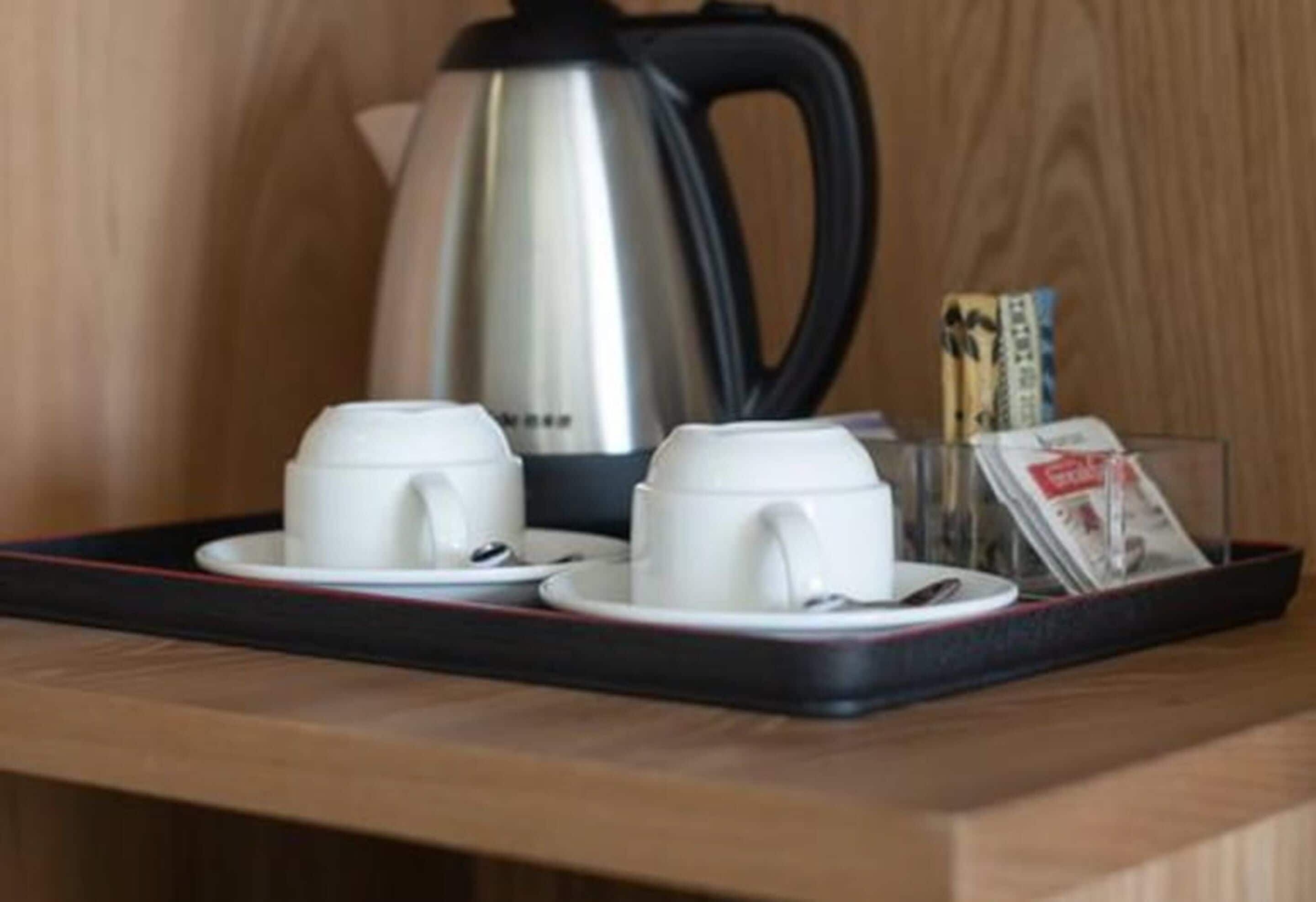 A tray with two white cups and a kettle on a wooden surface.