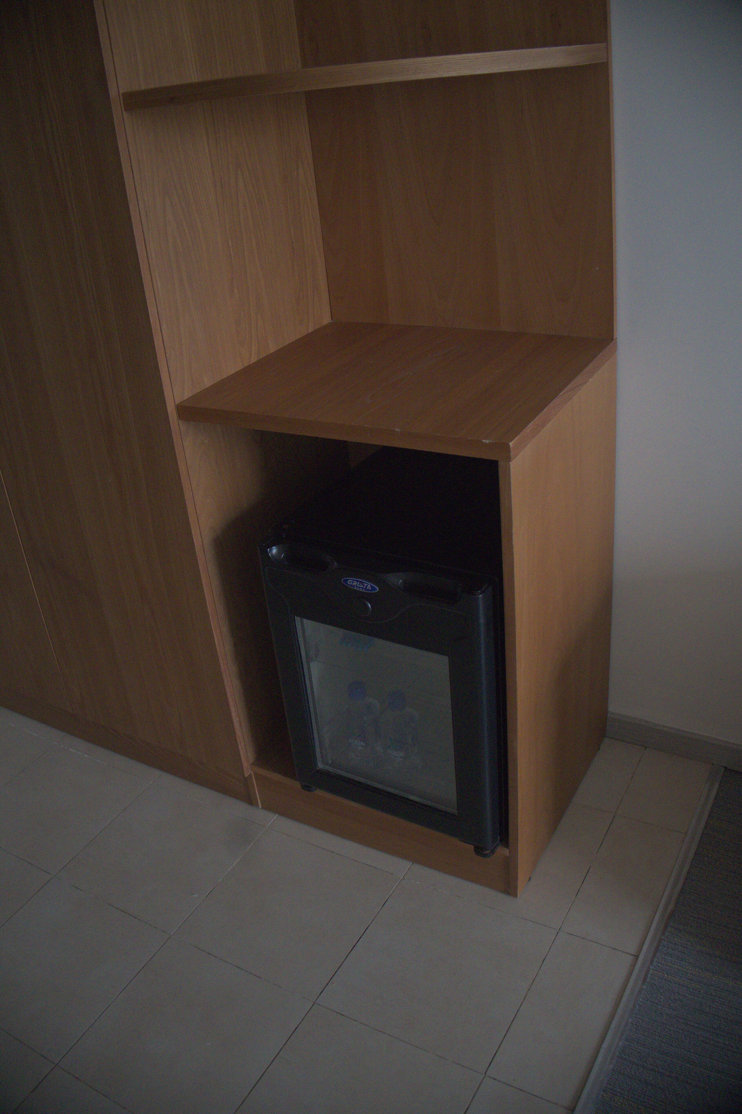 A corner of a room with a wooden cabinet and a black refrigerator.