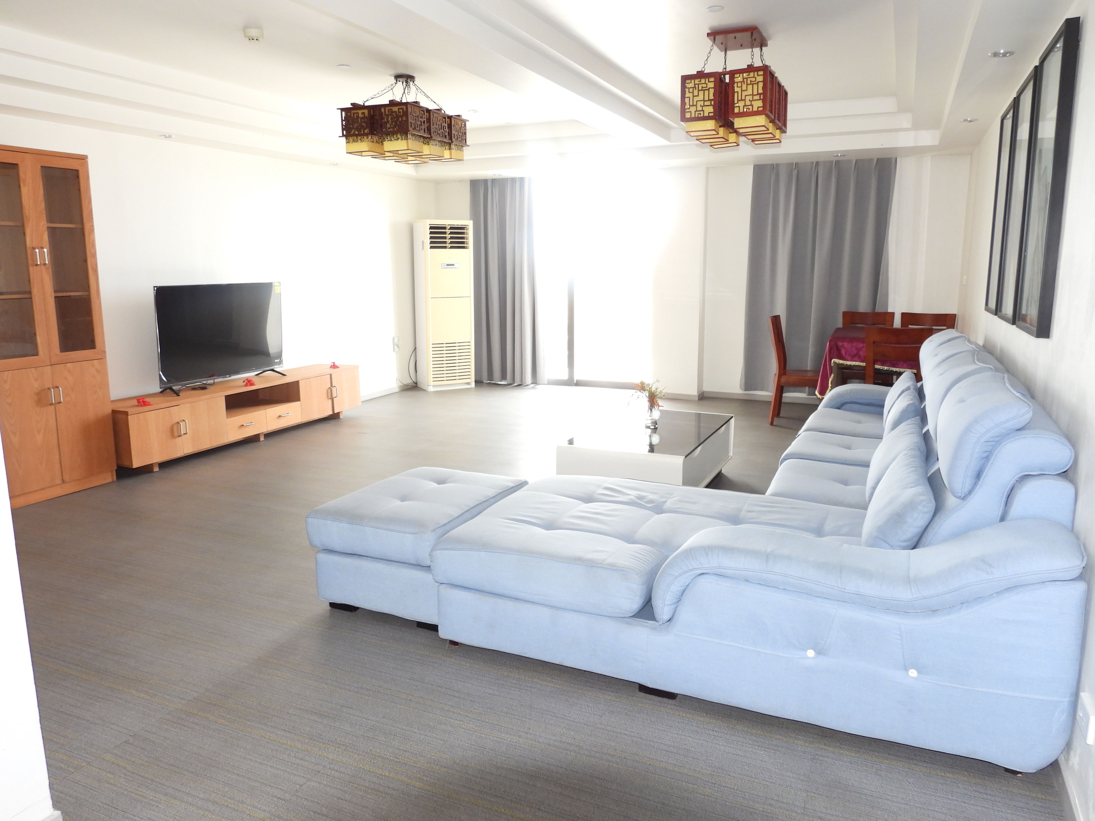 Een moderne woonkamer met een hoekbank, een flatscreen-tv, houten kasten en een eethoek met een tafel en stoelen.