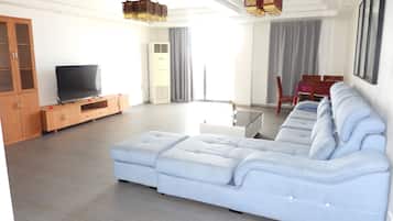 A modern living room with a sectional sofa, a flat-screen TV, wooden cabinets, and a dining area with a table and chairs.