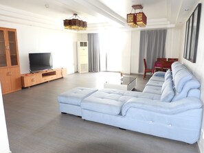 A modern living room with a sectional sofa, a flat-screen TV, wooden cabinets, and a dining area with a table and chairs. - Nalagi Hotel (Nadi)