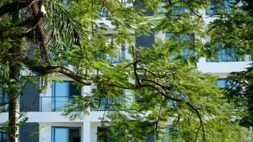A multi-story building with balconies and large windows, surrounded by lush greenery.