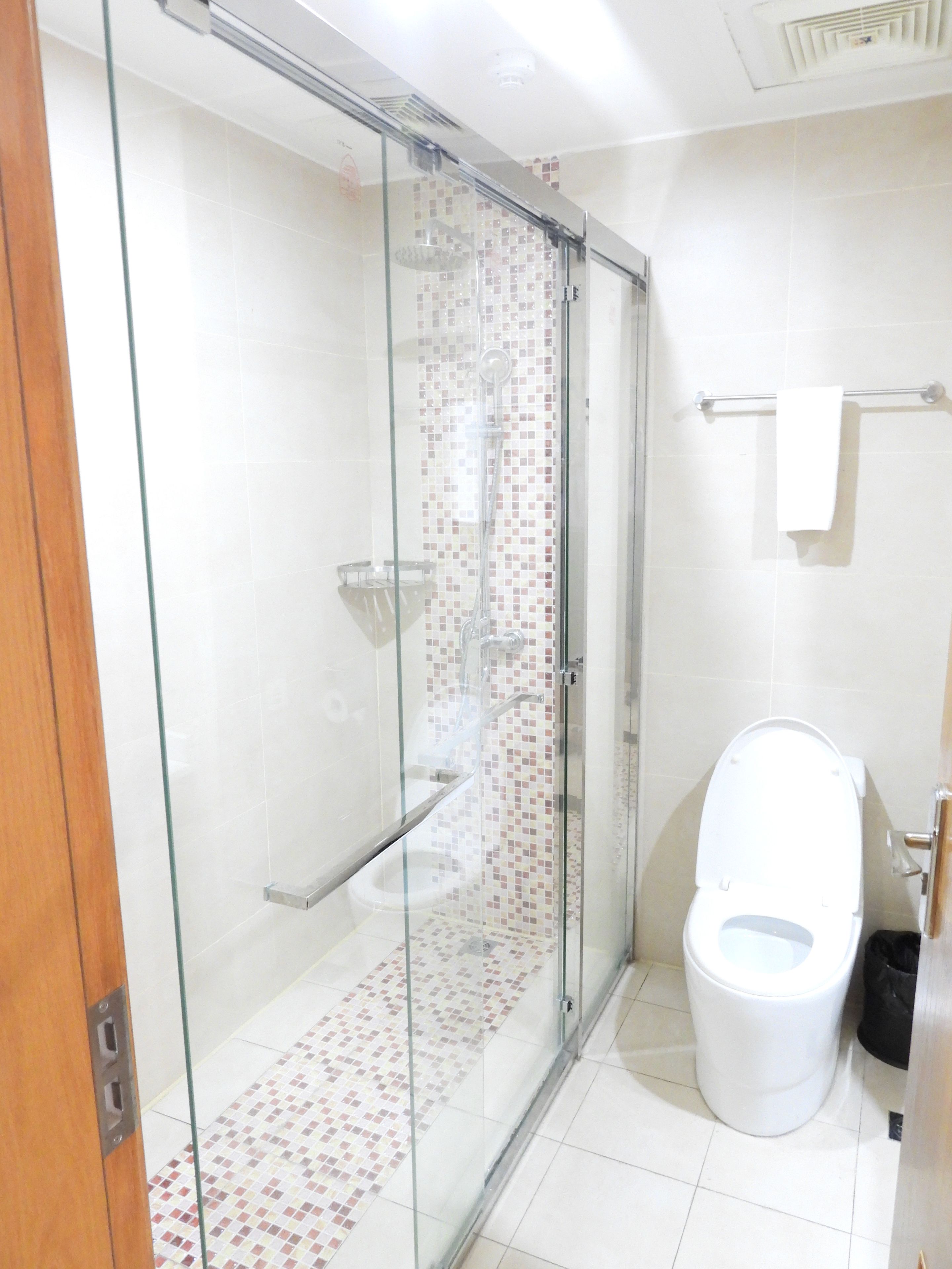 Un baño con ducha separada por mamparas de vidrio, inodoro y piso de baldosas.