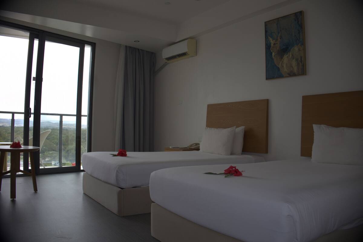 Une chambre d’hôtel avec deux lits, une table et une vue dégagée grâce à de grandes fenêtres.