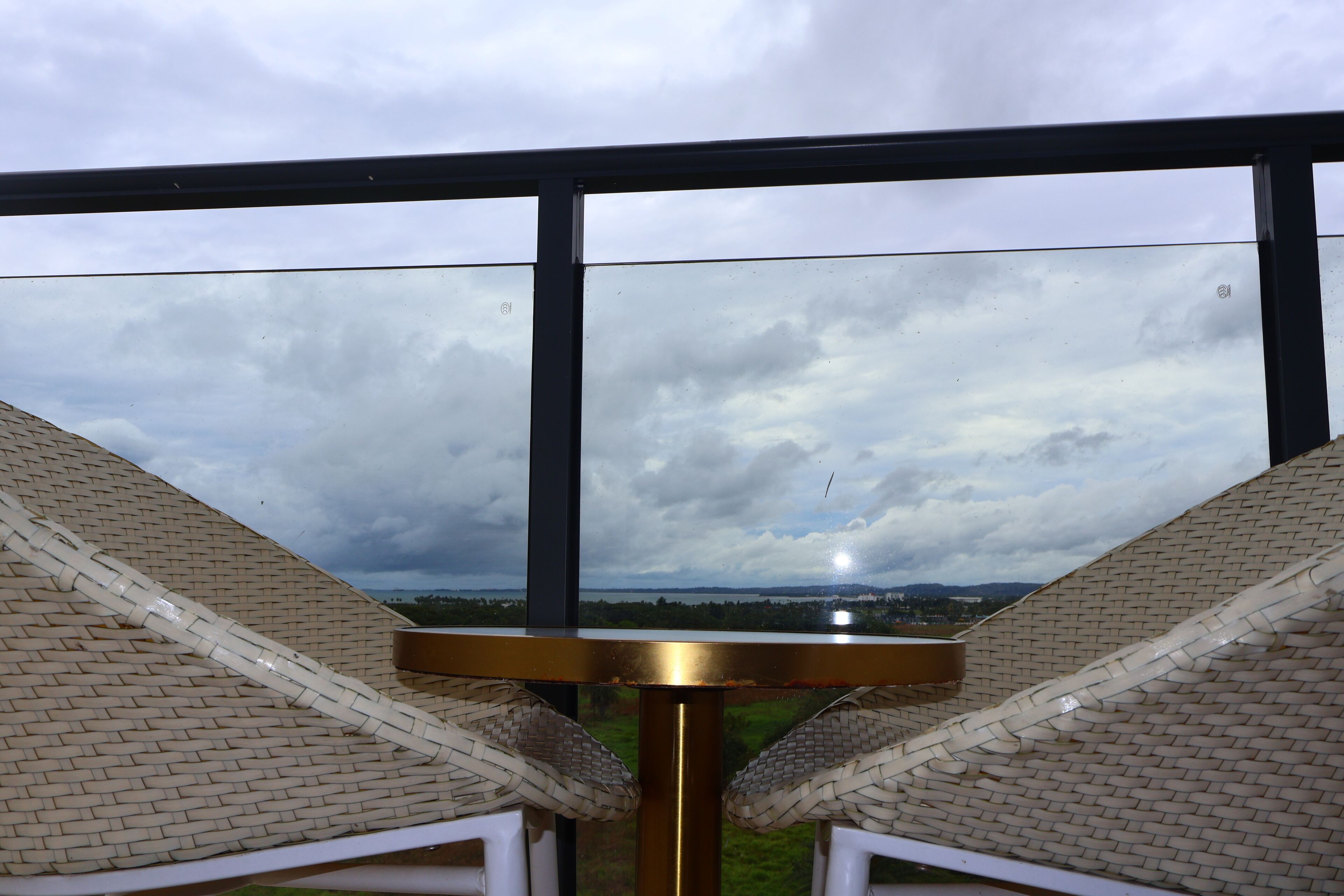 A view from a balcony with a metal railing, a woven chair, and a round table.
