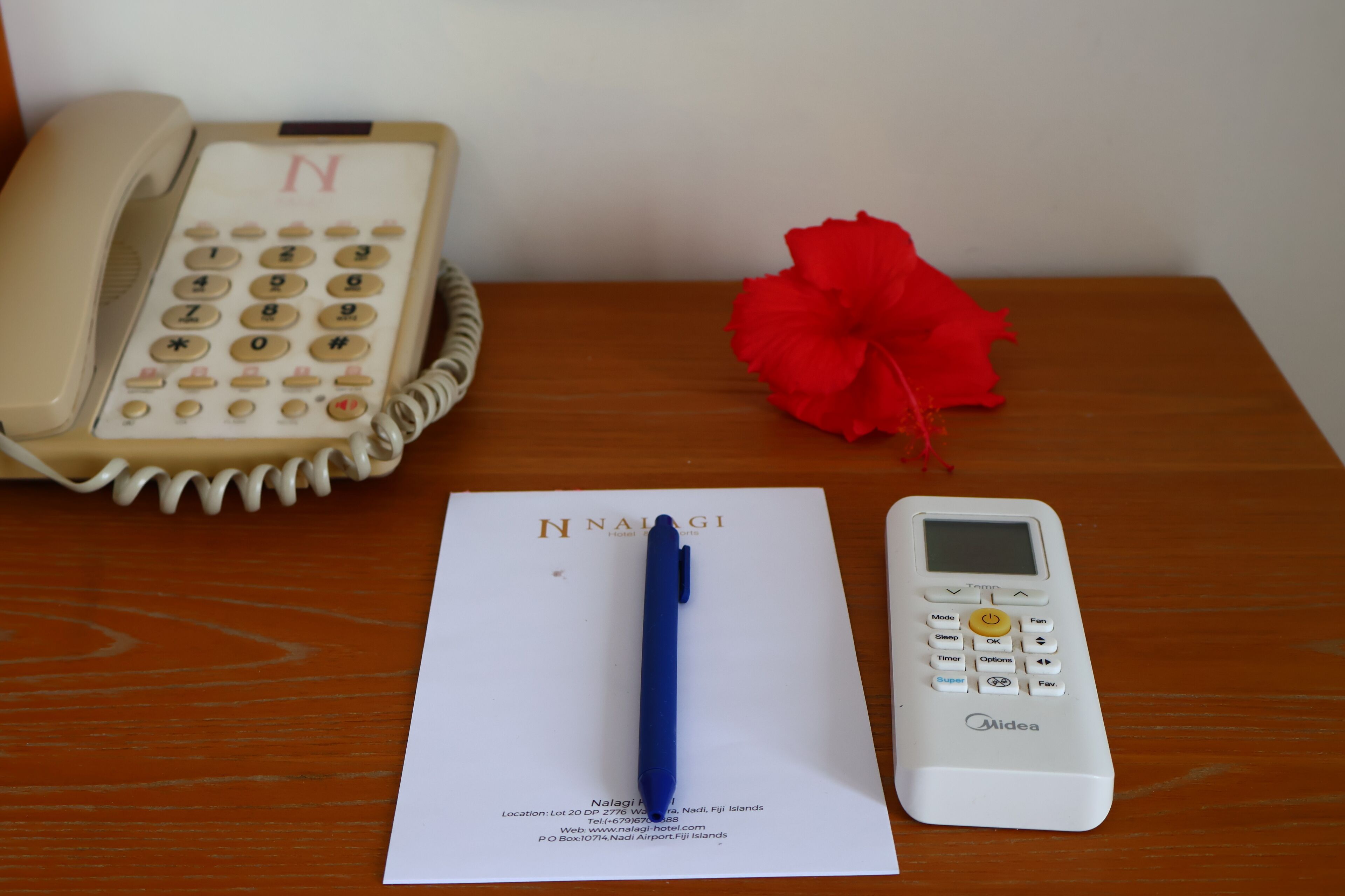Habitación de hotel con teléfono, bolígrafo, hoja de papel con detalles del hotel y una flor roja.