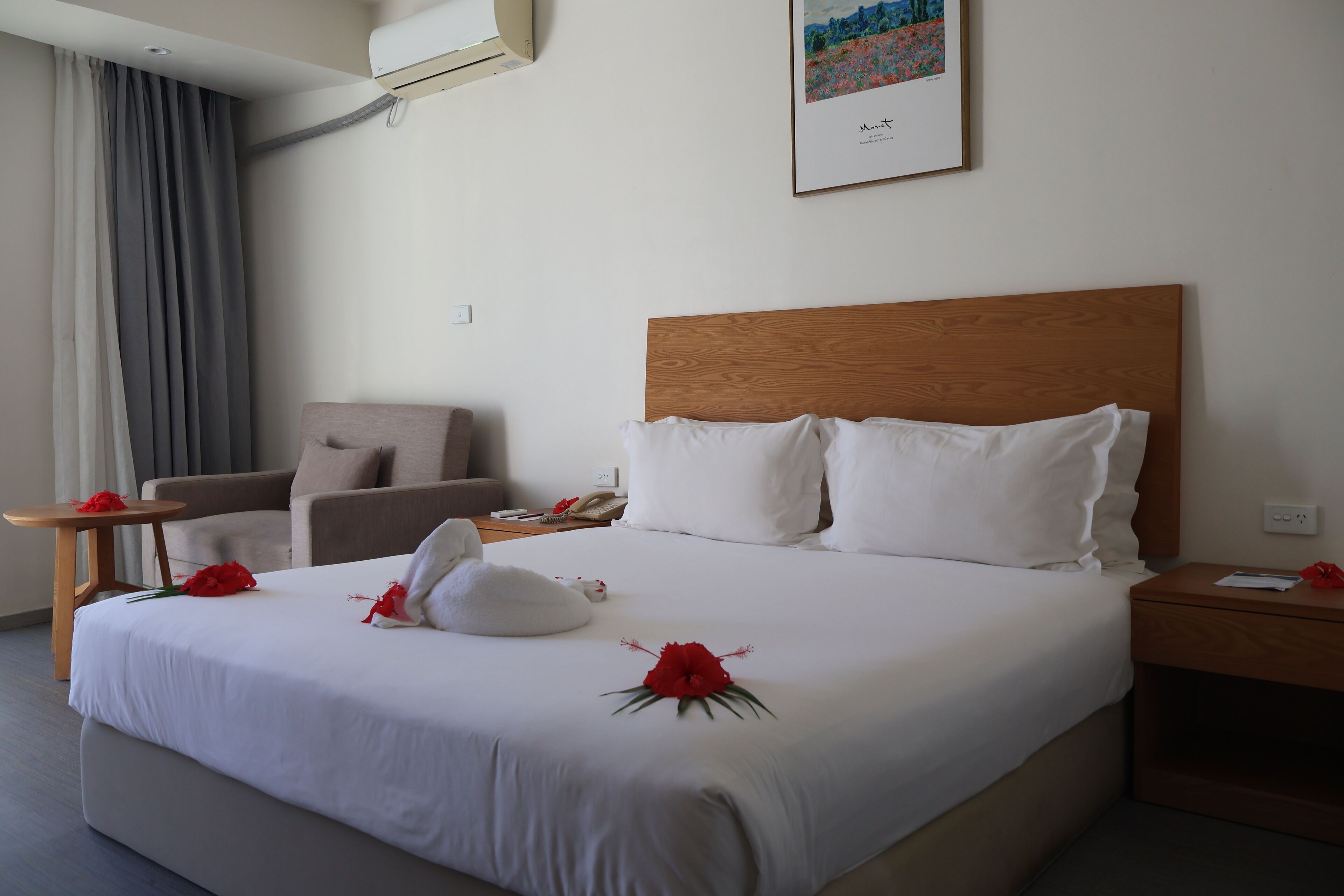 A hotel room with a large bed, a wooden headboard, a small table, a chair, and a painting on the wall.