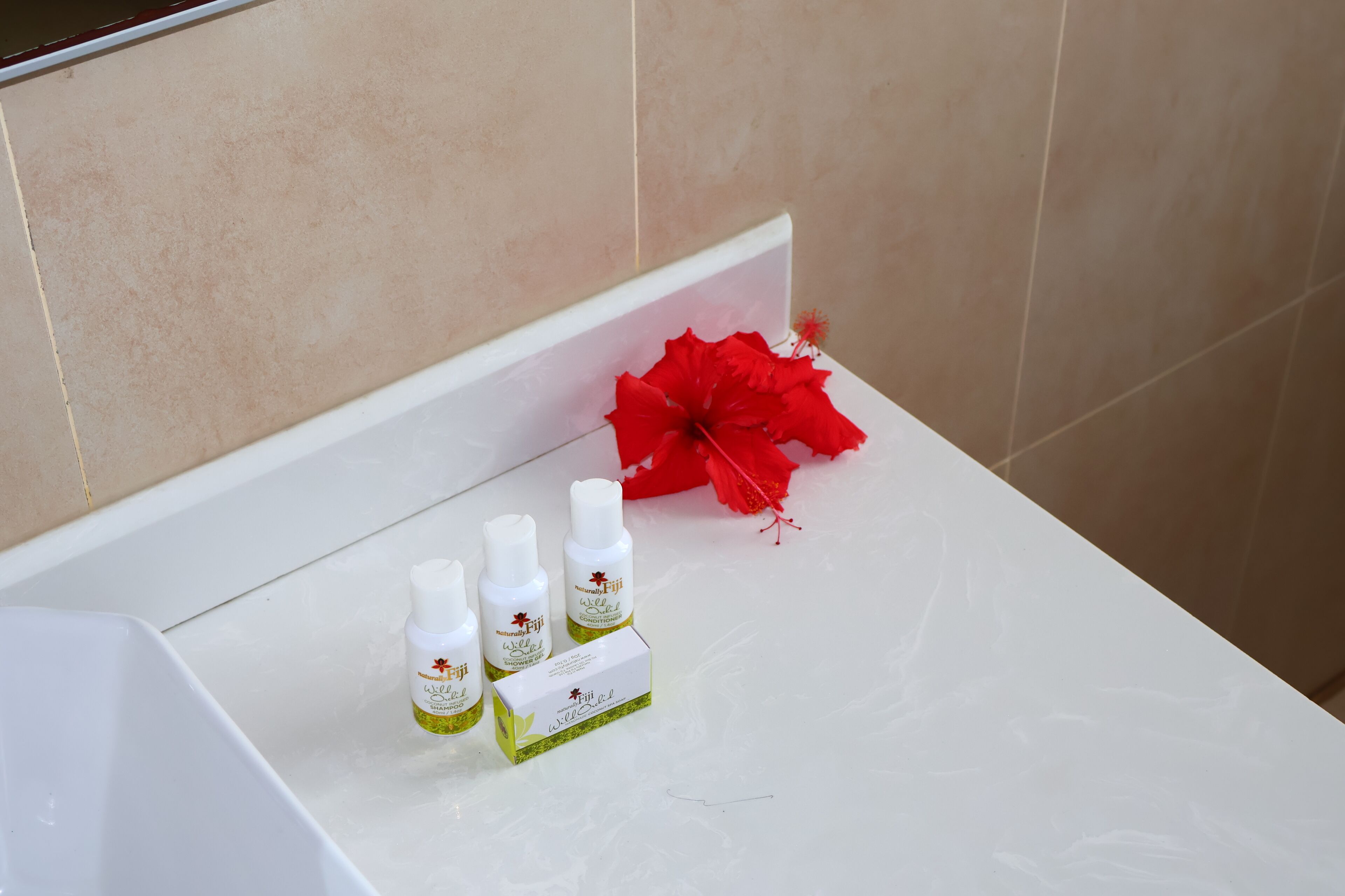 A bathroom with a white bathtub, three bottles of Fiji shower gel, and a red hibiscus flower on the edge.
