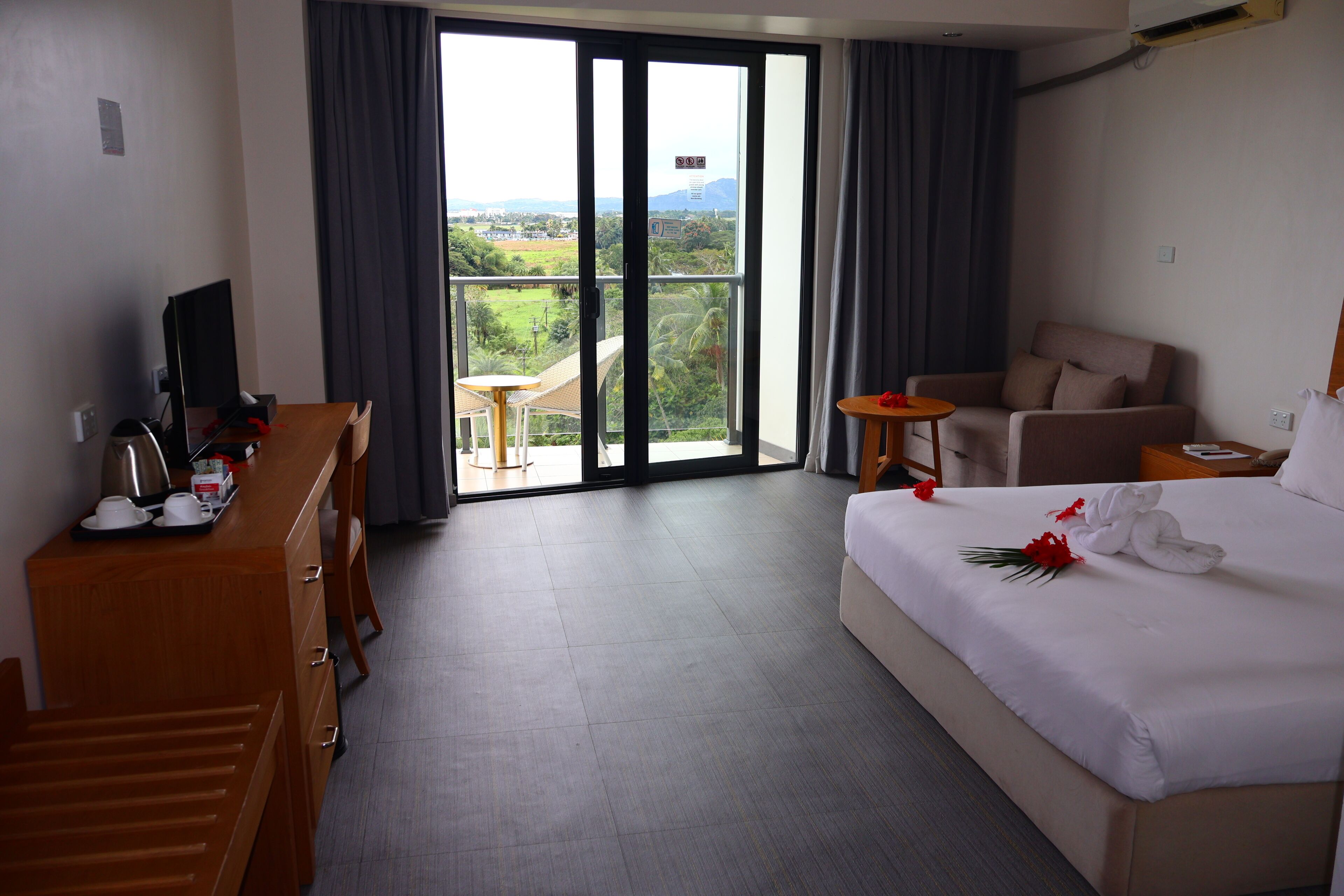 Une chambre d’hôtel comprenant un lit, un bureau avec un ordinateur, une chaise, une petite table et une vue sur l’extérieur grâce à une porte coulissante.