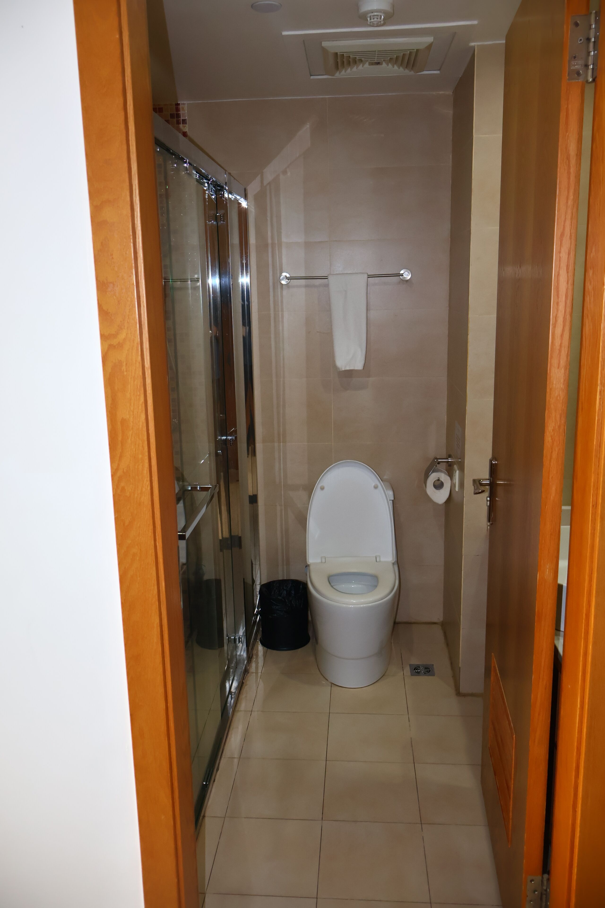 Un baño pequeño con inodoro, cabina de ducha de vidrio y una toalla en un perchero.