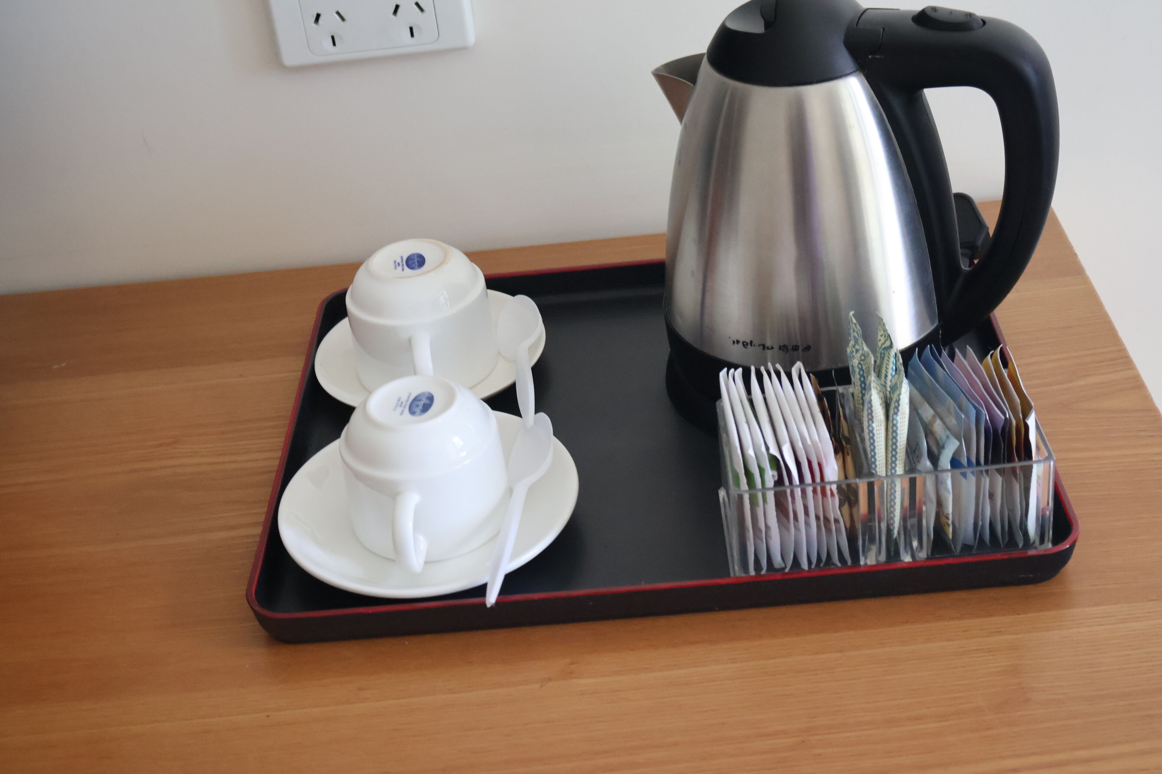 A tray with a teapot, two cups, and a stack of magazines on a wooden table.