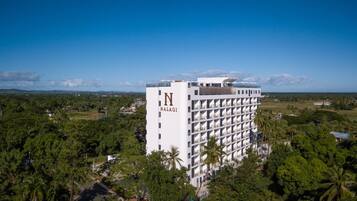 A high-rise hotel with a prominent 'N' logo on the side, surrounded by lush greenery and a clear blue sky.