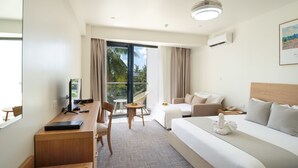A hotel room with a bed, a desk, a chair, a small table, and a balcony with curtains.
