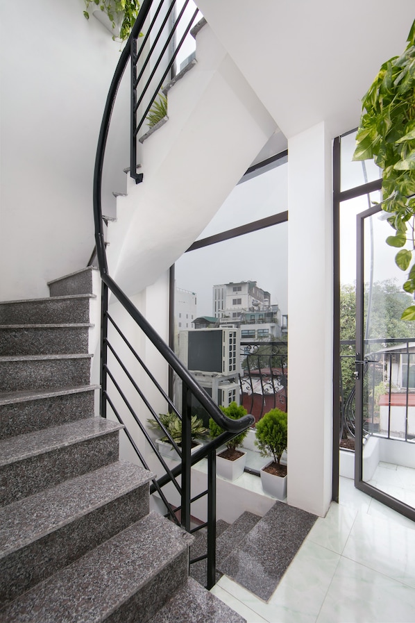 A modern staircase with granite steps and black railings, leading to a balcony with potted plants and a view of buildings.