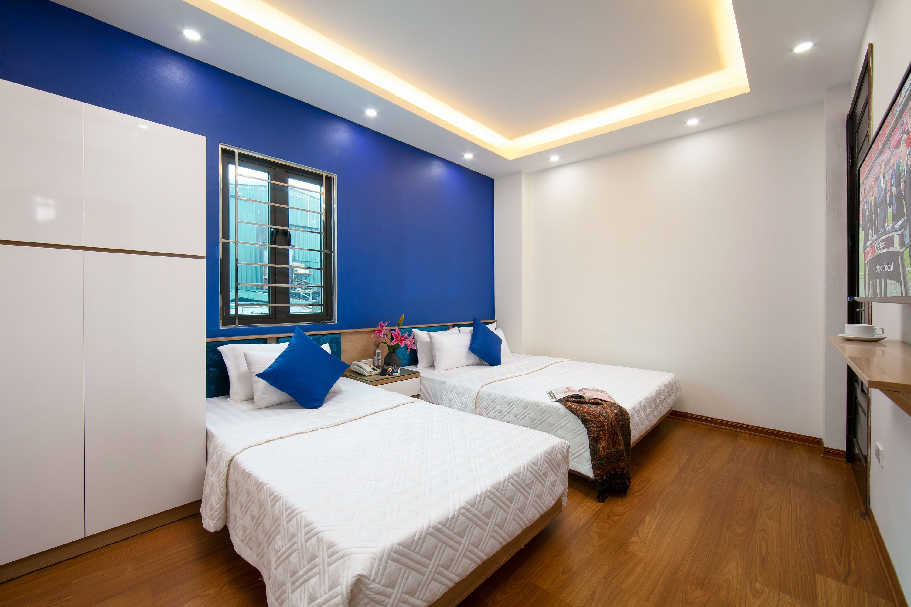 A hotel room with two beds, a window, and a kitchenette.
