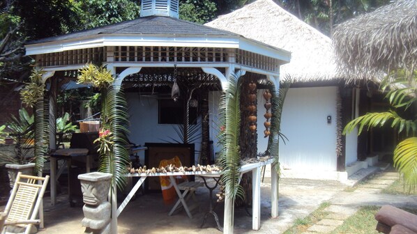 Un kiosque doté d’un toit de chaume, entouré de plantes tropicales et orné d’une statue en pierre.