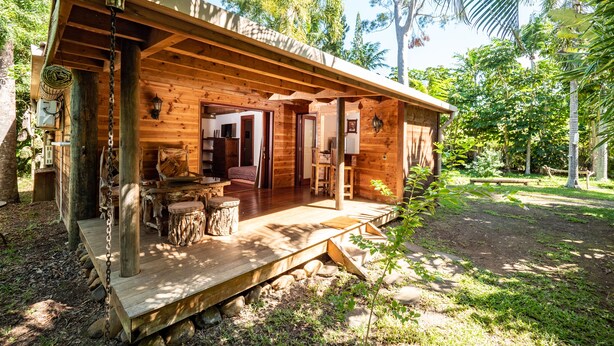 Eine Holzhütte mit Veranda, eingebauten Sitzgelegenheiten und Blick auf den umliegenden Wald.