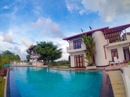 A swimming pool with a two-story building, a tree, and a clear sky.