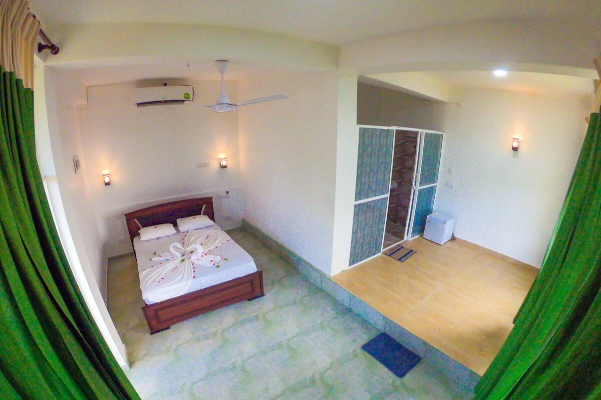 Un dormitorio con cama, ventilador de techo, aire acondicionado instalado en la pared y puerta corredera que da a un balcón.