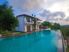 A two-story house with a swimming pool, surrounded by lush greenery and a cloudy sky.