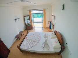 A bedroom with a bed, a wooden bench, a mirror, a ceiling fan, and a view of the outdoors.
