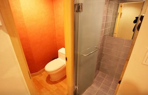 A bathroom with a glass shower enclosure, a white toilet, and a tiled floor. - We Motel (Pyeongchang)