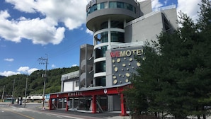 Un motel moderno con un diseño arquitectónico único, que presenta una torre circular y un llamativo letrero 'WEMOTEL'.